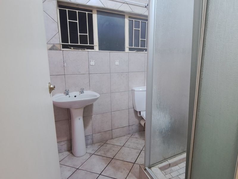A functional bathroom featuring a pedestal basin, toilet, and shower enclosure with tiled finishes, requiring cosmetic updates to modernize the space.