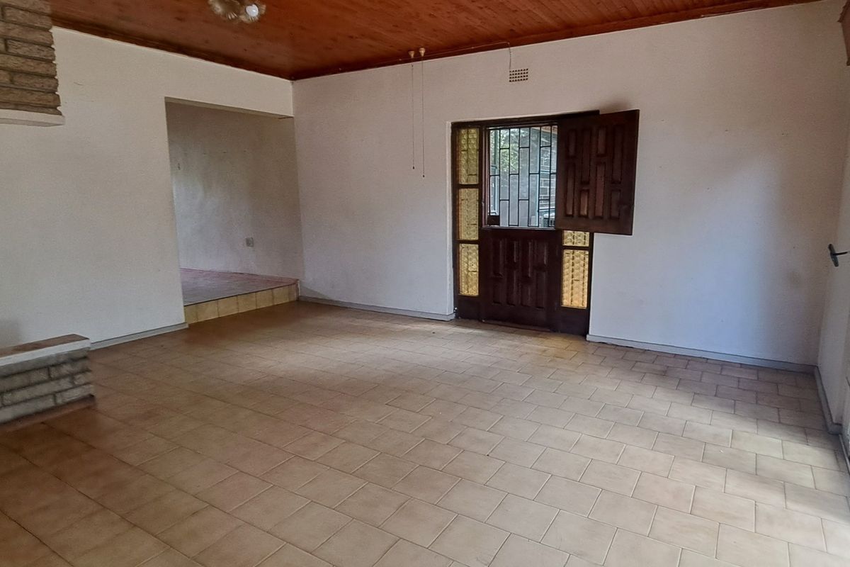 Spacious living area featuring a brick fireplace, timber ceiling, and tiled flooring, with direct access to the exterior through a security gate and sliding door.
