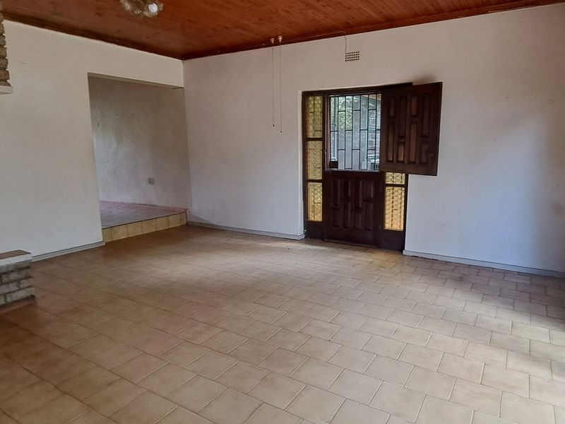 Spacious living area featuring a brick fireplace, timber ceiling, and tiled flooring, with direct access to the exterior through a security gate and sliding door.