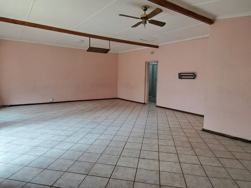 A spacious, empty living area featuring tiled flooring, exposed ceiling beams, and a ceiling fan, offering a blank canvas for interior design.