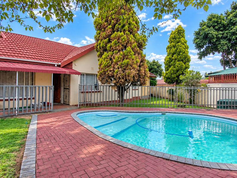 Outdoor pool area featuring a swimming pool, red brick paving, and metal security fencing, set against the rear elevation of the house.