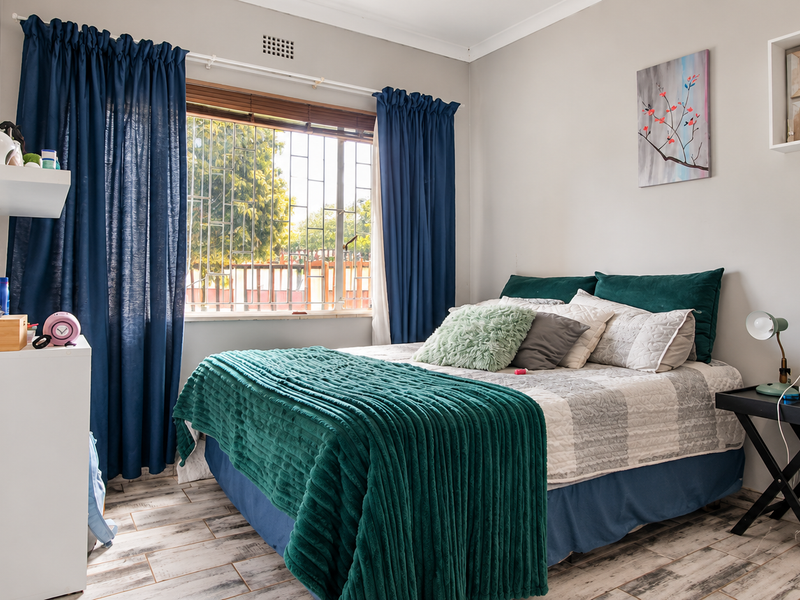 A well-maintained bedroom featuring laminate flooring, security bars on the window, and built-in wall shelving.
