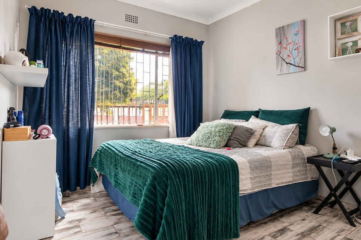 A well-maintained bedroom featuring laminate flooring, security bars on the window, and built-in wall shelving.
