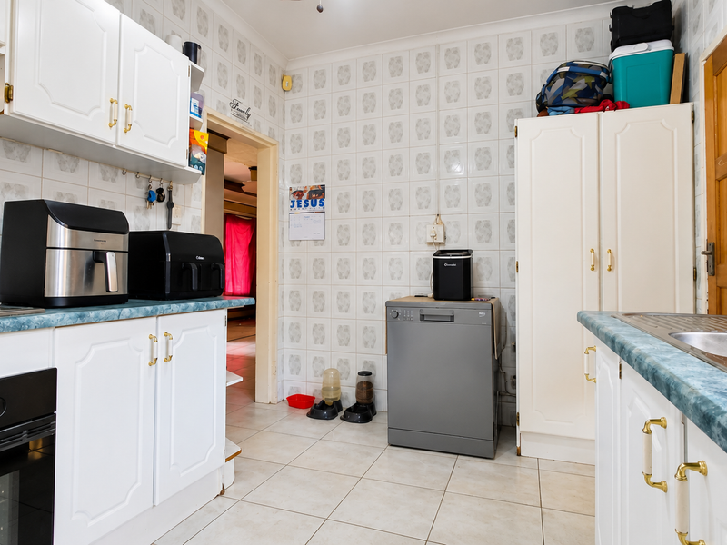 A functional kitchen featuring white cabinetry, a gas hob with extractor, double sink, and tiled finishes throughout.