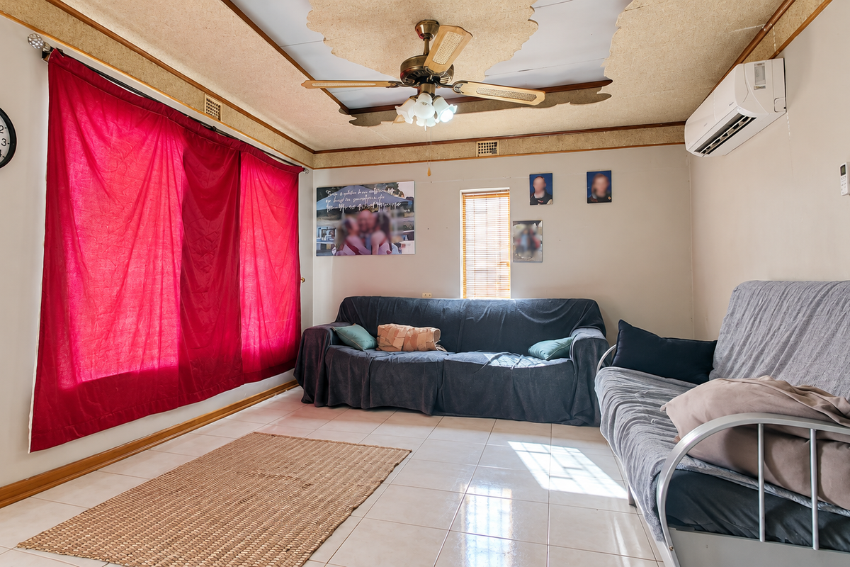 Living room featuring tiled flooring, a ceiling fan, and a wall-mounted split-system air conditioner. The ceiling requires repair and cosmetic attention.
