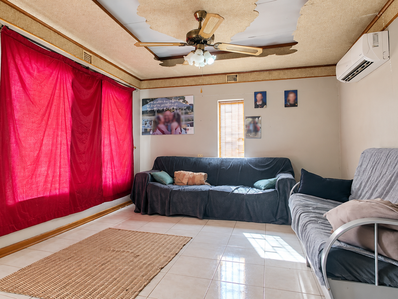 Living room featuring tiled flooring, a ceiling fan, and a wall-mounted split-system air conditioner. The ceiling requires repair and cosmetic attention.