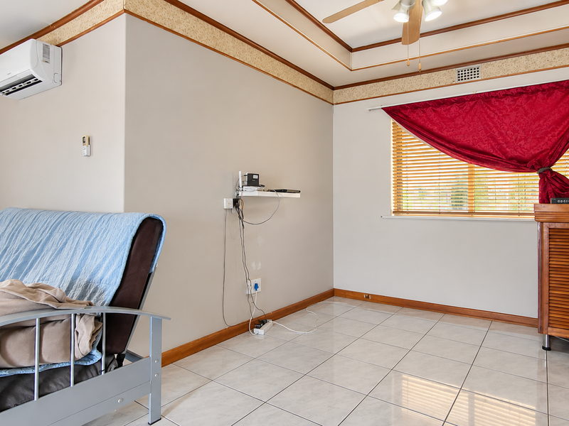 A living area featuring tiled flooring, a ceiling fan, and a wall-mounted split-system air conditioner, with neutral walls and decorative ceiling trim.