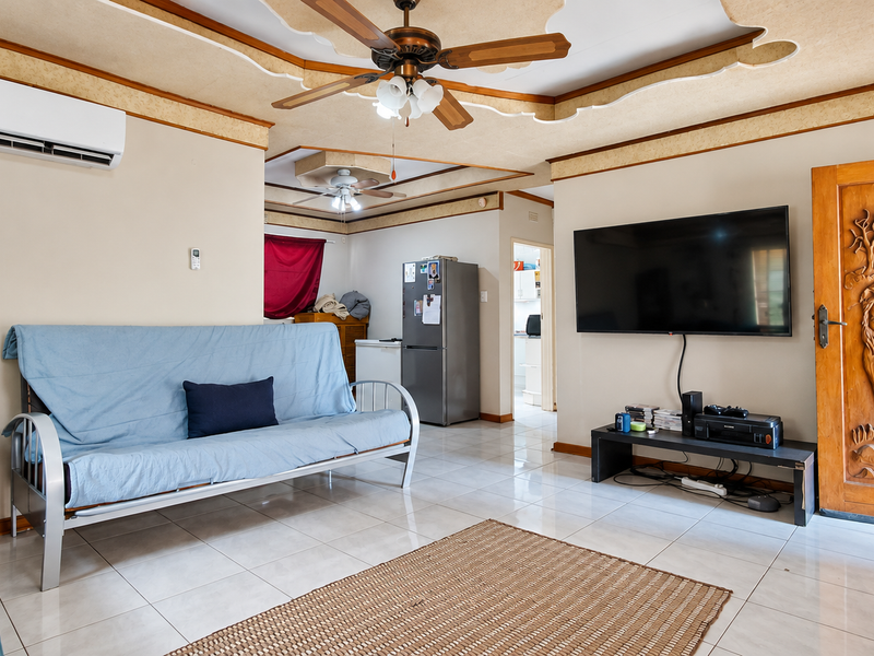 Open-plan living area featuring tiled floors, a split-system air conditioner, ceiling fan, and a decorative carved wooden door leading to other areas.