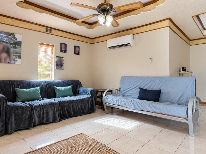 A living room featuring tiled flooring, a ceiling fan, and a wall-mounted split-system air conditioner.