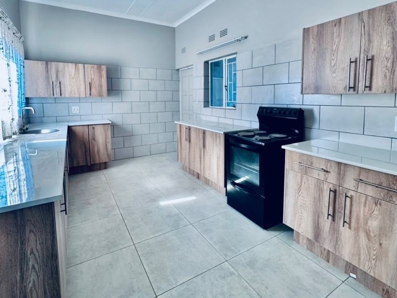 A clean, modern kitchen featuring wood-look cabinetry, stone-look countertops, tiled splashbacks, and a freestanding electric stove in a bright, open layout.