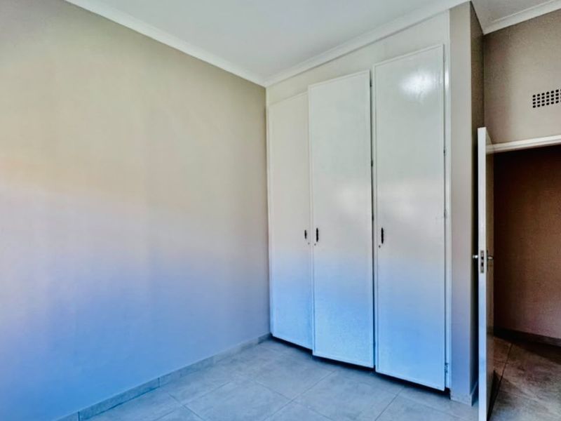 An empty bedroom featuring neutral wall tones, tiled flooring, and white built-in cupboards, offering a clean and versatile space.