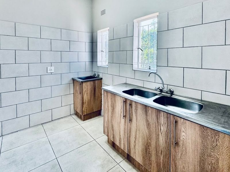 A clean and functional laundry room featuring double and single stainless steel sinks, wood-look cabinetry, and modern tiled finishes.