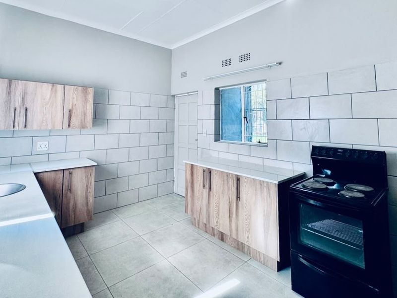 A clean, modern kitchen featuring light wood-finish cabinetry, white tiled backsplash, tiled flooring, and a freestanding stove with ample counter space.