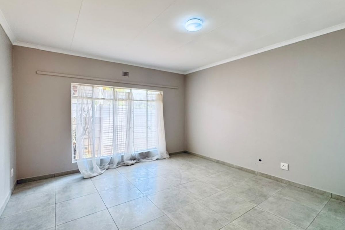 A bright and spacious empty bedroom featuring neutral wall tones, large window for natural light, and clean tiled flooring throughout.