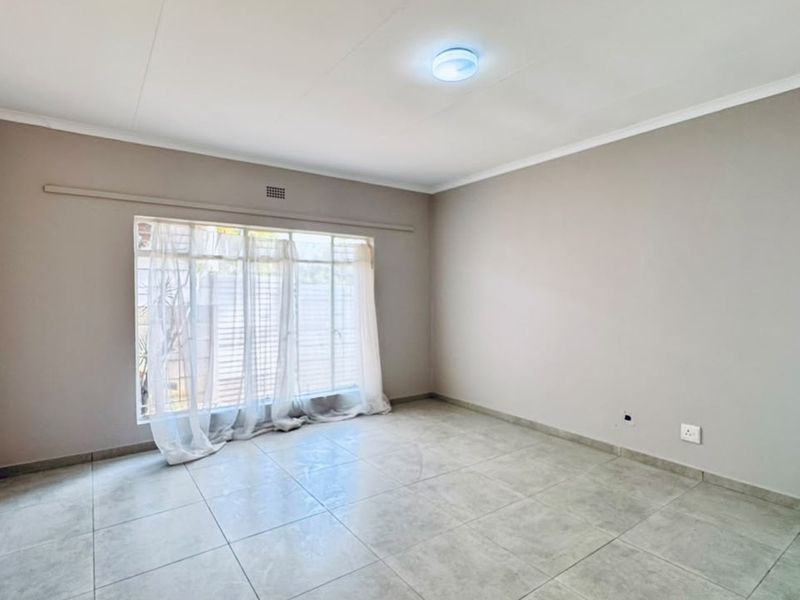 A bright and spacious empty bedroom featuring neutral wall tones, large window for natural light, and clean tiled flooring throughout.