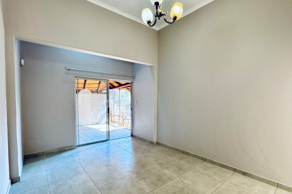 A bright, empty living room featuring neutral tiled flooring, a classic ceiling light fixture, and a sliding glass door providing access to an outdoor patio.