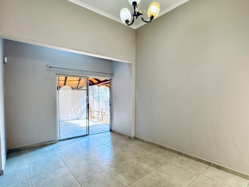A bright, empty living room featuring neutral tiled flooring, a classic ceiling light fixture, and a sliding glass door providing access to an outdoor patio.