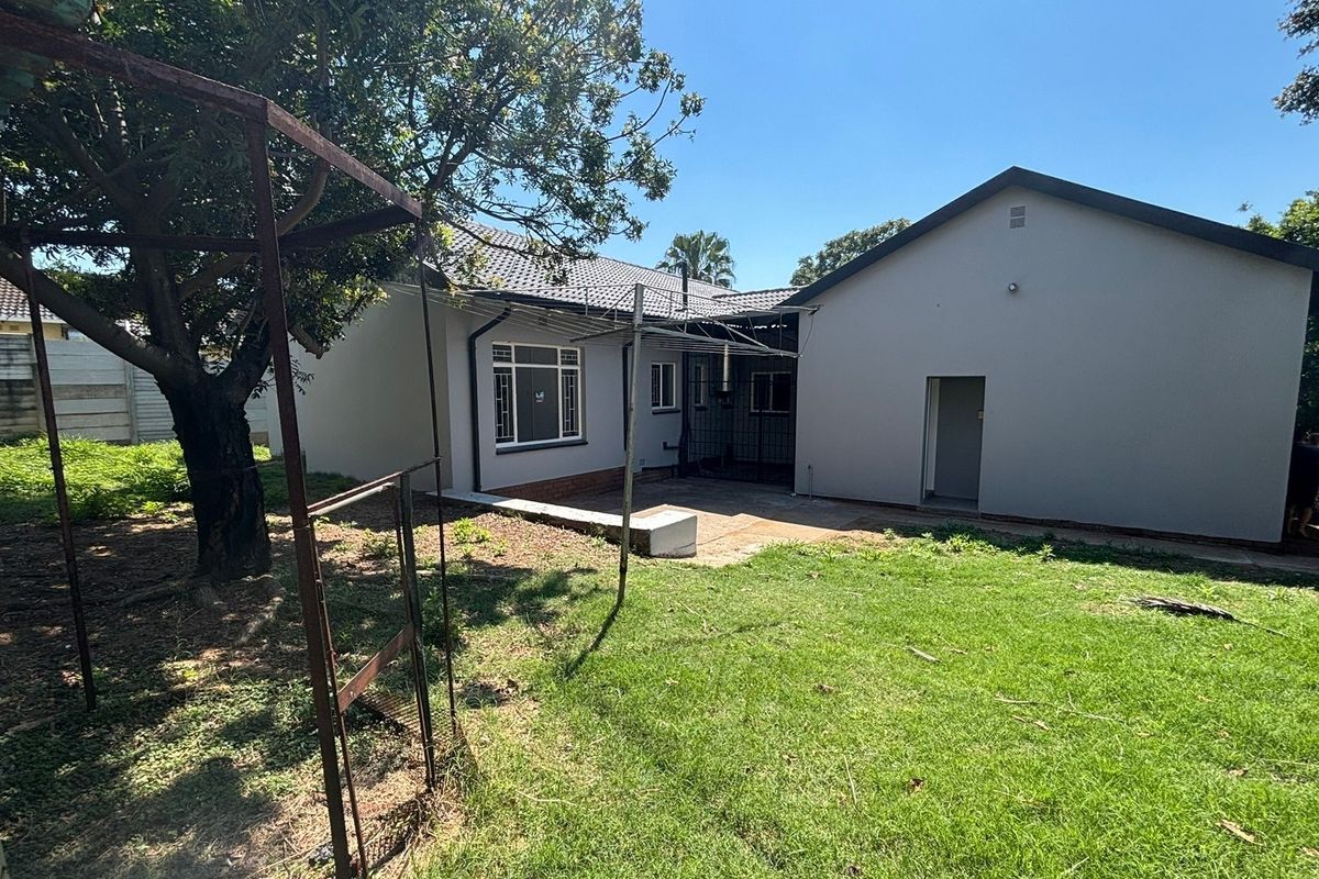 Rear view of the house featuring a concrete patio area, tiled roof, and a spacious garden with mature trees.