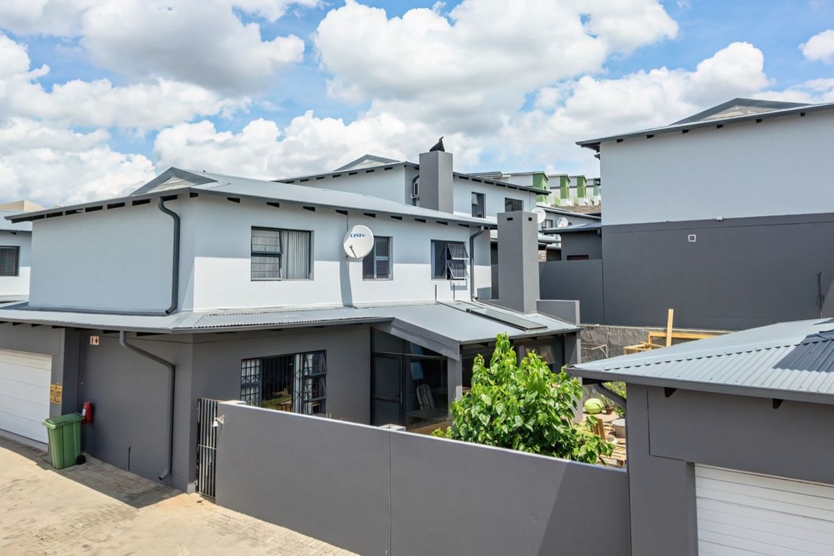 Rear view of a modern two-story residential property featuring a corrugated metal roof, chimney, and secure boundary wall with a private garage entrance.