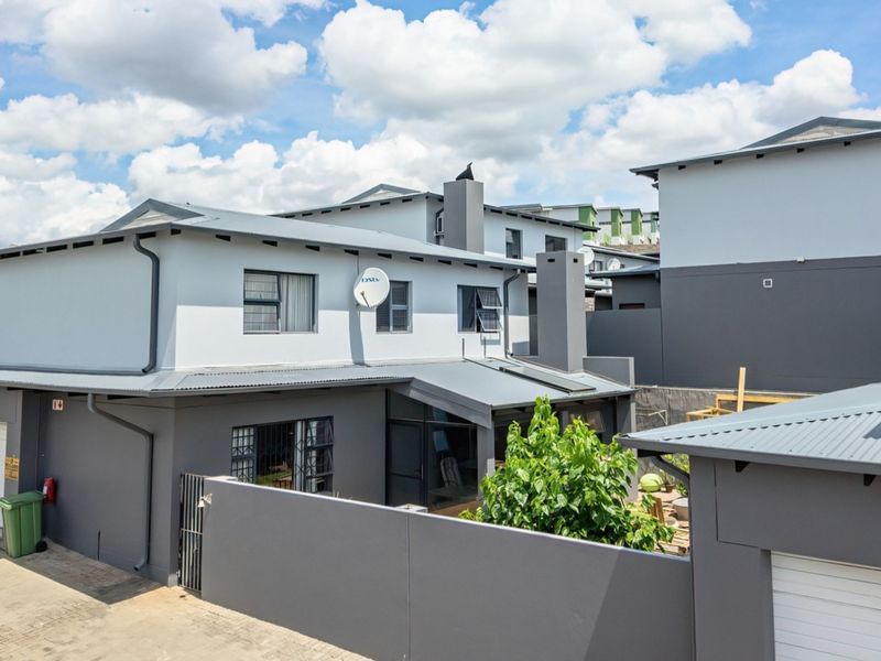Rear view of a modern two-story residential property featuring a corrugated metal roof, chimney, and secure boundary wall with a private garage entrance.