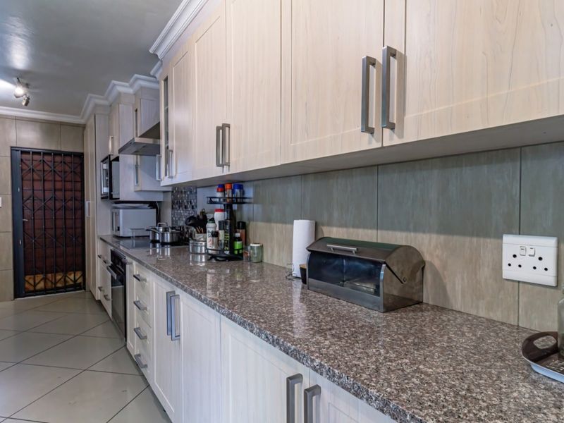 A functional kitchen featuring light wood-finish cabinetry, granite countertops, tiled flooring, and integrated appliances, with direct access to an exterior security door.