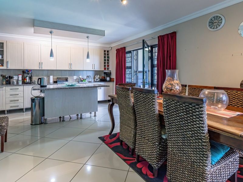 Spacious open-plan kitchen and dining area featuring light-toned cabinetry, granite countertops, tiled flooring, and direct access to the outdoor patio area.