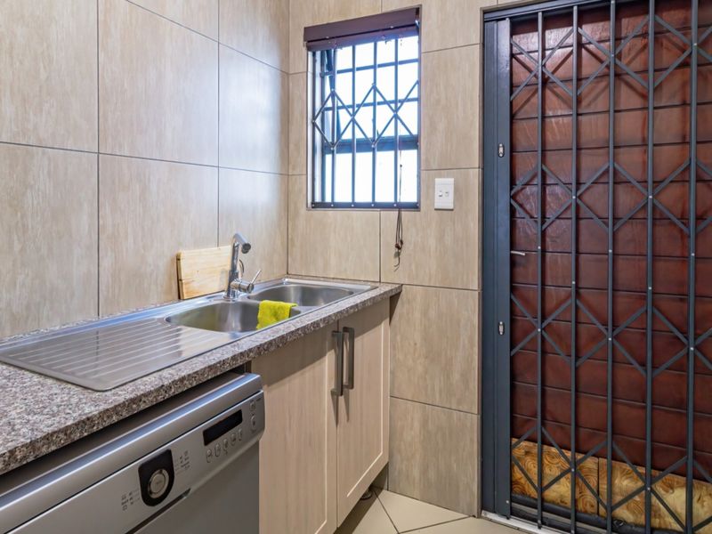 A functional scullery area featuring a stainless steel sink, granite countertop, built-in cabinetry, and a secure entrance door with a metal security gate.