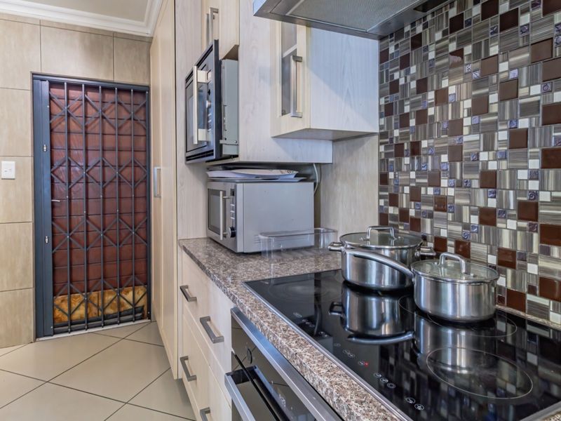 Modern kitchen featuring granite countertops, mosaic tile backsplash, built-in oven, electric hob, and extractor fan, with tiled flooring and a secure exterior door.