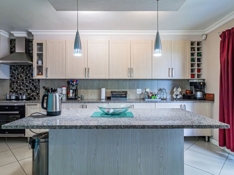 A well-maintained kitchen featuring light wood cabinetry, granite countertops, a central island, and integrated appliances, offering a functional and clean cooking space.