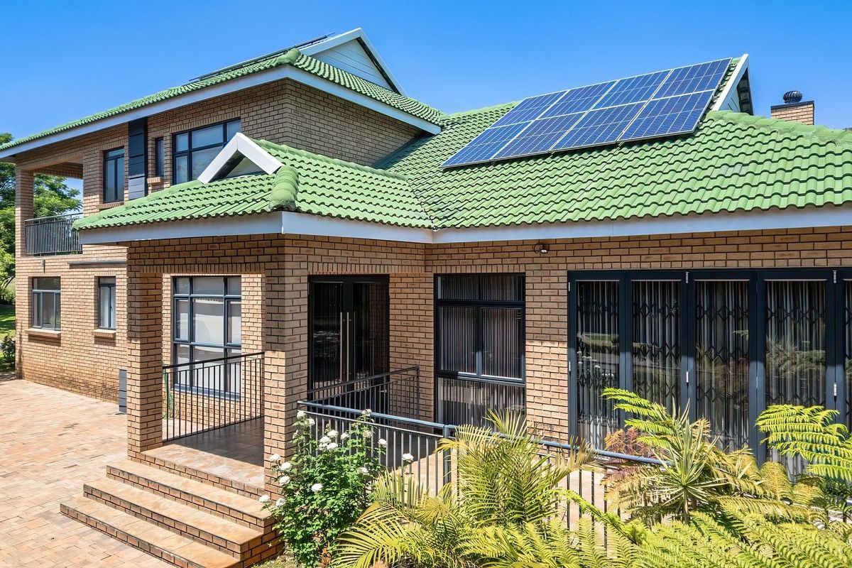 Rear view of a double-storey brick house featuring a green tiled roof with solar panels, a paved patio area, and secure aluminium window frames.