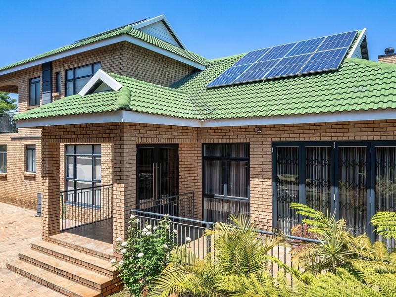 Rear view of a double-storey brick house featuring a green tiled roof with solar panels, a paved patio area, and secure aluminium window frames.