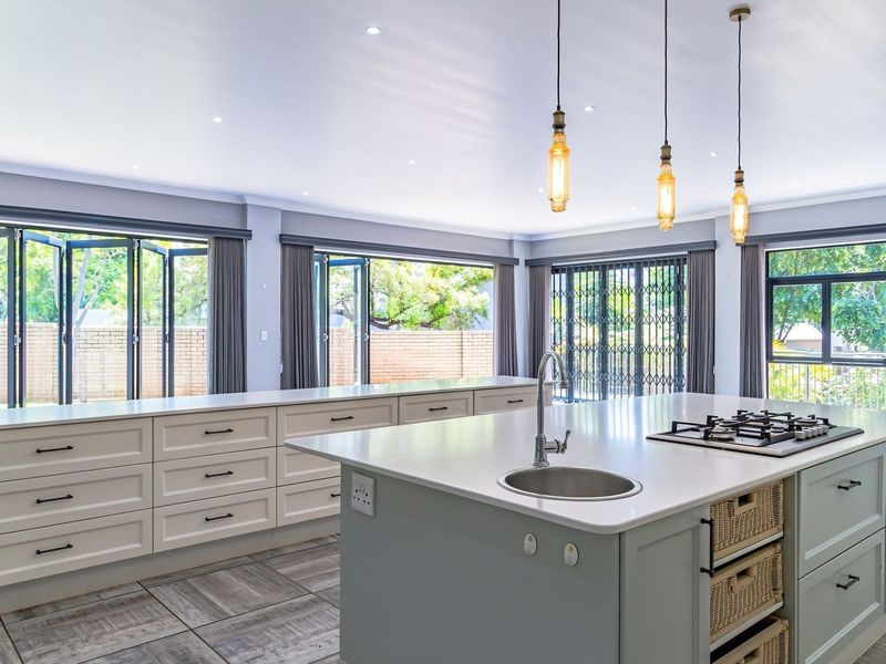 Spacious modern kitchen featuring a large central island with gas hob, stone countertops, shaker cabinetry, and expansive bi-fold doors opening to the garden.