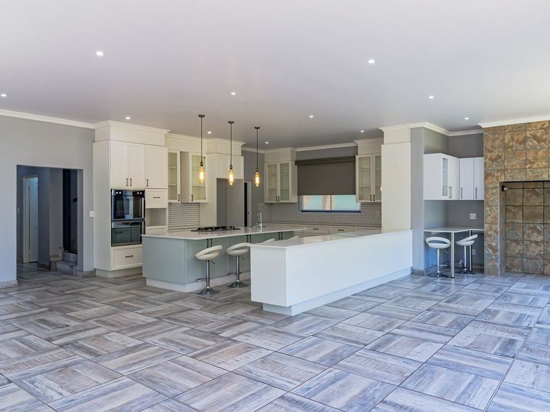 Spacious open-plan kitchen featuring a large island, built-in oven, gas hob, and modern tiled flooring, seamlessly integrated with a tiled feature wall.