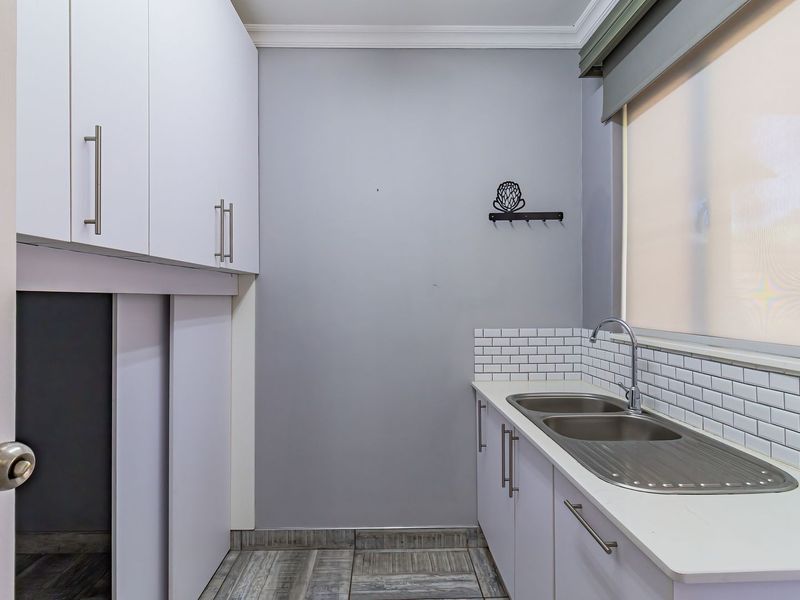 A clean and functional scullery featuring built-in cabinetry, a double stainless steel sink, subway tile backsplash, and modern tiled flooring.