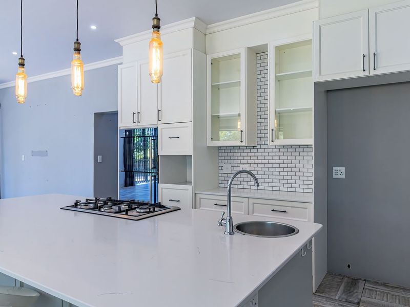 Modern kitchen featuring a large island with a gas hob and sink, white cabinetry, subway tile backsplash, and stylish pendant lighting.