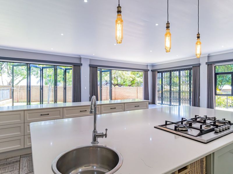 Modern, spacious kitchen featuring a large island with a gas hob, quartz countertops, shaker cabinetry, and expansive folding glass doors leading to the exterior.