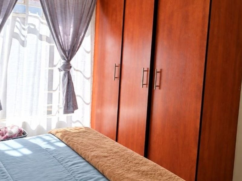 A bedroom featuring a large, full-height built-in wooden wardrobe and natural light from the window.