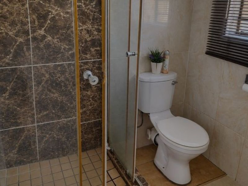 A functional bathroom featuring a glass-enclosed shower with marble-effect tiling, a standard toilet, and neutral wall tiles.