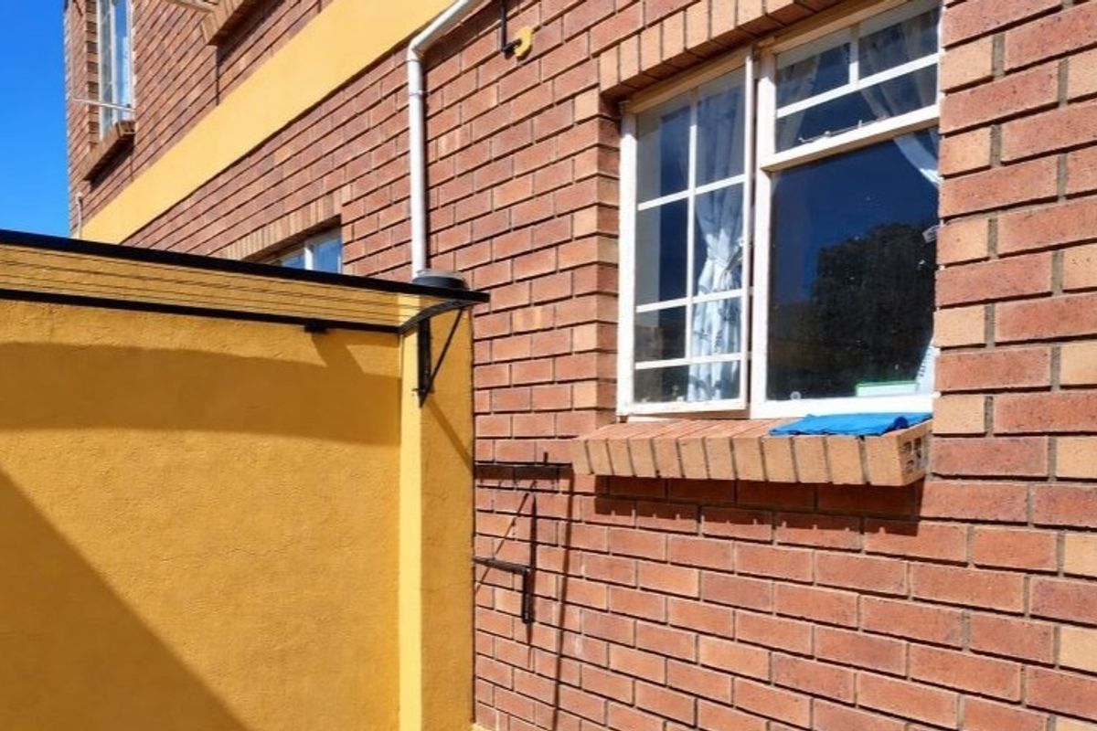 A view of the exterior rear facade featuring face brick walls, security bars on the windows, and a small protective awning.