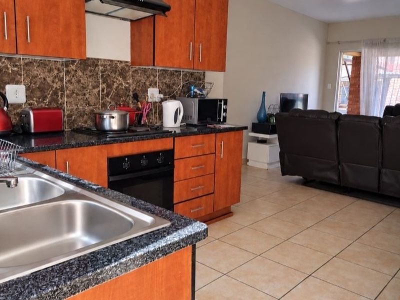 Open plan kitchen and living area featuring wooden cabinetry, granite countertops, built-in oven, hob, and tiled flooring throughout.