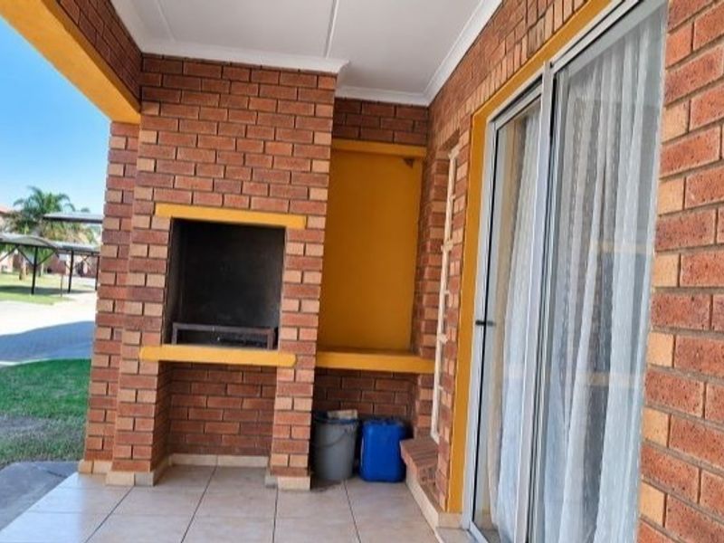 Covered patio area featuring a built-in brick braai, tiled flooring, and direct access to the interior through sliding glass doors.