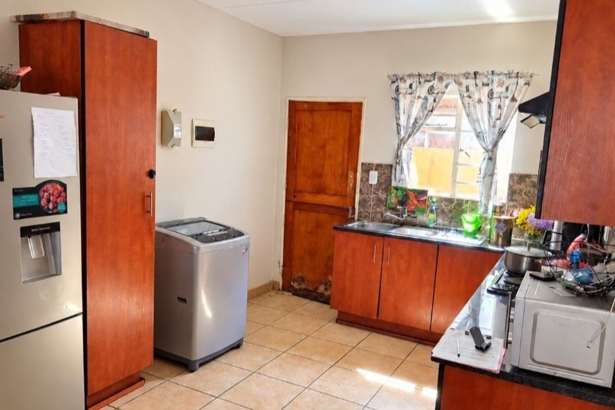 A functional kitchen featuring wooden cabinetry, tiled flooring, and a double sink, with some visible wear on the door and cabinetry finishes.