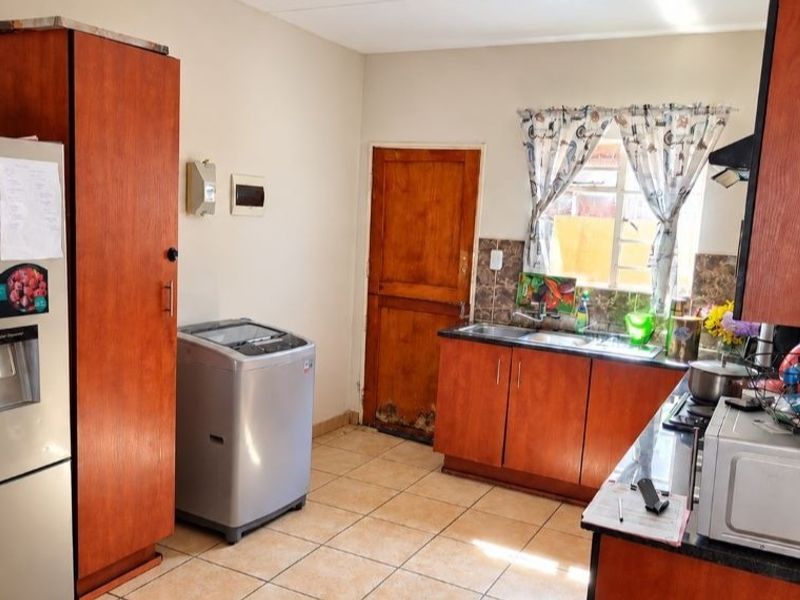 A functional kitchen featuring wooden cabinetry, tiled flooring, and a double sink, with some visible wear on the door and cabinetry finishes.