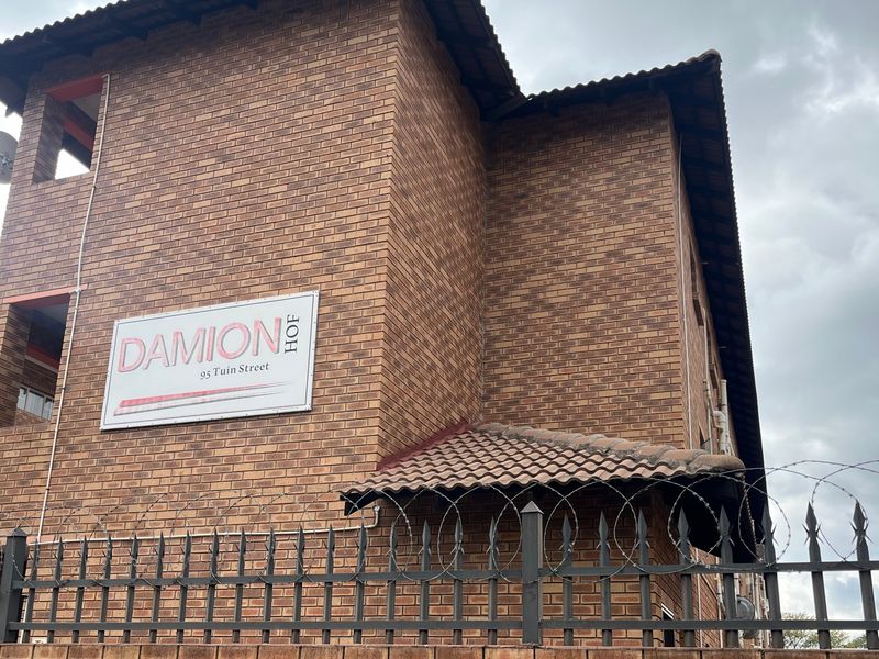 Exterior view of the Damion Hof apartment complex featuring a face brick facade, tiled roof, and secure perimeter fencing.