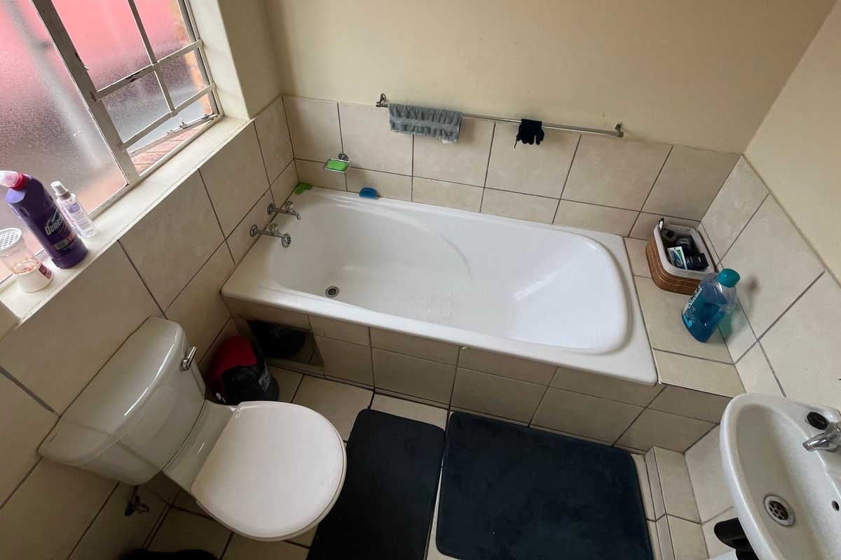A functional bathroom featuring a built-in bathtub, pedestal basin, and toilet, finished with neutral ceramic wall and floor tiling.