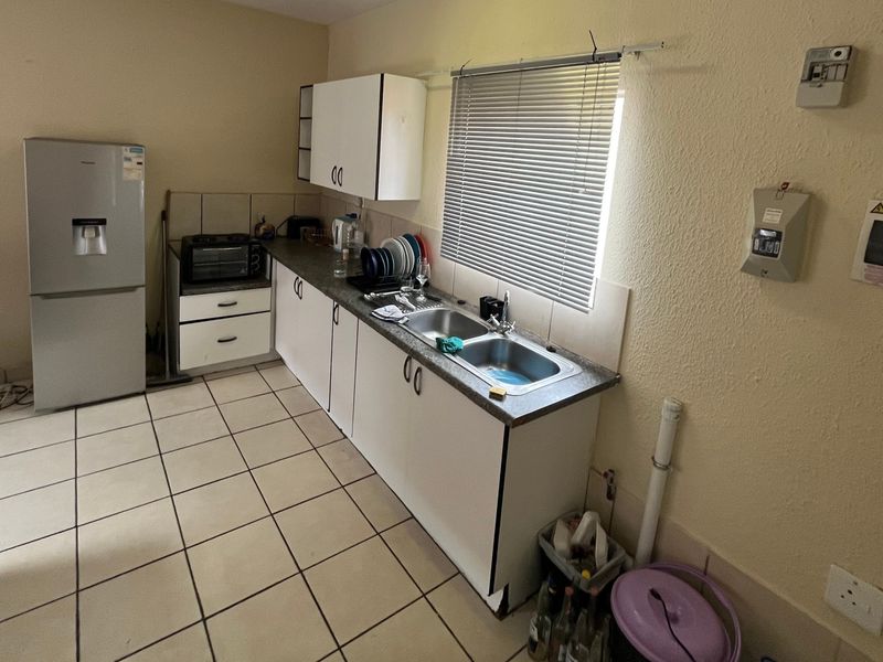 A functional kitchen featuring laminate countertops, a double basin sink, built-in cabinetry, and tiled flooring, requiring some maintenance and cosmetic updates.