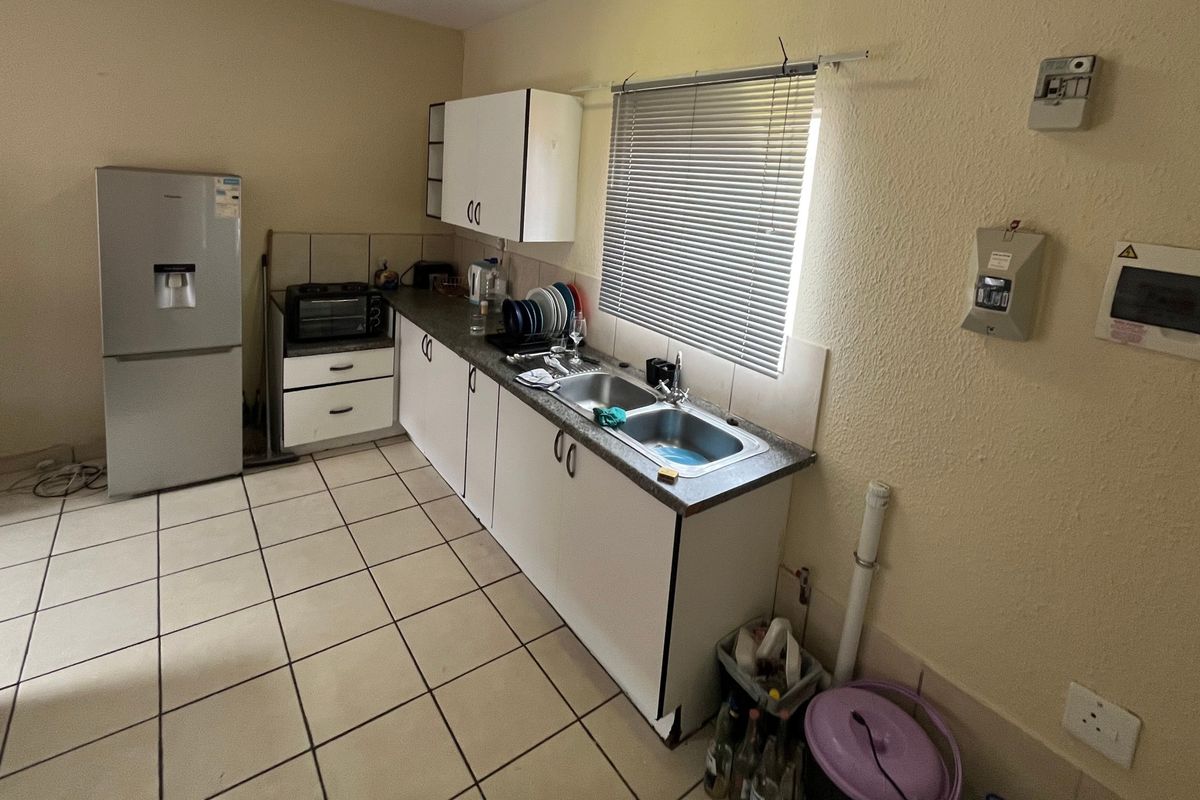 A functional kitchen featuring laminate countertops, a double basin sink, built-in cabinetry, and tiled flooring, requiring some maintenance and cosmetic updates.