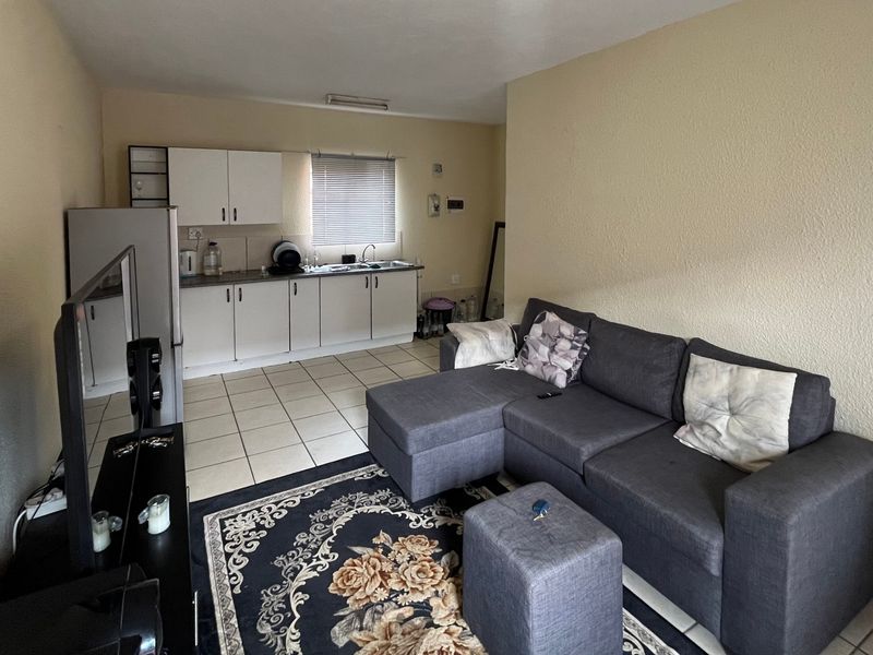 Open-plan living area featuring a functional kitchen with white cabinetry and tiled flooring, seamlessly connected to the lounge space.