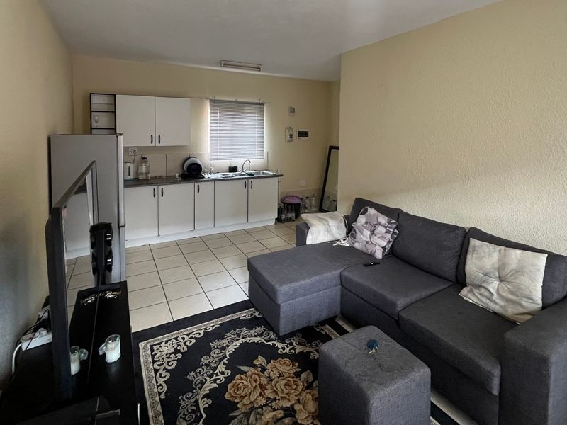 Open-plan living area featuring a functional kitchen with built-in cabinetry, sink, and tiled flooring throughout the space.