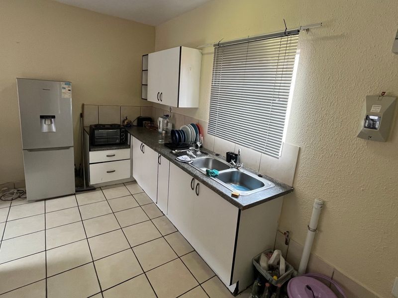 A functional kitchen featuring tiled flooring, laminate countertops, a double sink, and built-in cabinetry, offering potential for modernization and aesthetic improvement.